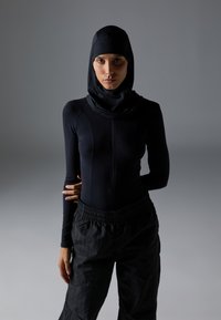 Svart atletisk langermet topp med høy krage og integrert hijab, kombinert med løse svarte bukser, på en nøytral bakgrunn.