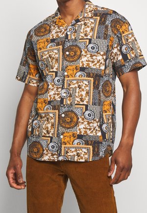 Mann trägt ein kurzärmeliges Hemd mit einem mehrfarbigen abstrakten geometrischen und floralen Muster in Orange-, Schwarz-, Weiß- und Brauntönen.