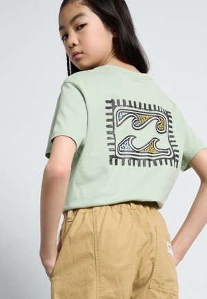 T-shirt di cotone verde chiaro con un audace grafico astratto a onde in nero, giallo e blu sul retro; maniche corte e vestibilità rilassata.