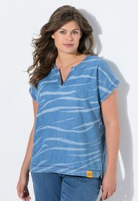 Top in denim blu chiaro con scollo a V, maniche corte e motivo a strisce di tigre bianche. Patch logo giallo all'orlo. Vestibilità casual e rilassata.