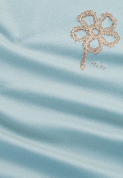 Lyseblåt stof med en glat overflade, der prydes af en beige broderet blomstedesign samt "NN. 07" detalje nederst til højre.