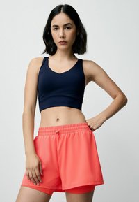 Sötétkék crop top v-nyakkivágással és ujjatlan fazonnal, világos korall színű, laza szabású rövidnadrággal, amely elasztikus derékkal és zsinórral rendelkezik.
