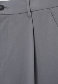 Pantalones grises plisados hechos de tela texturizada, con cierre de botones y trabillas para cinturón. Costuras detalladas alrededor de los bolsillos y la pretina.