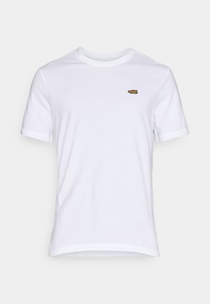 Bílá bavlněná tričko, klasický střih, kratké rukávy, s malým hnědým vyšitým logem boty na levé části hrudi.