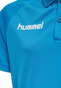 Blå polo-shirt i mjukt tyg, med klassisk krage, tre knappar och en framträdande vit "hummel"-logotyp på vänster bröst.