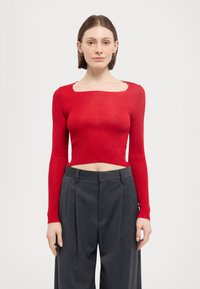 Red ribbed long-sleeve cropped top with a square neckline paired with high-waisted gray pleated trousers. Smooth texture and fitted style.