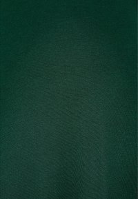 Tumma vihreä kangas, jossa on sileä pinta ja johdonmukainen kudontakuviot. Materiaali näyttää kevyeltä ja laskeutuu pehmeästi.