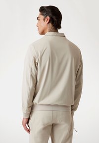 Beige letvægtsjakke med en afslappet pasform, lange ærmer og ribbet kant. Glat tekstur, krave detaljer og matchende bukser.