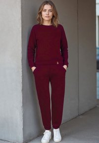 Set di felpa e joggers color bordeaux realizzato in tessuto morbido, con polsini a costine e un piccolo etichetta con il marchio, abbinato a sneakers bianche.