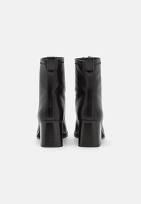 Bottes noires en cuir à talon carré, avec une texture lisse, fermeture éclair sur le côté et détails de couture à l'arrière.