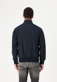 Giacca zip-up blu navy con colletto alto, polsini e orlo a costine, realizzata in tessuto liscio. Presenta maniche raglan per un design sportivo.