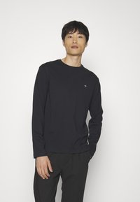 Lange mouwen zwarte shirt van gladde stof, met een ronde hals, aansluitende snit en een subtiele logo op de borst.