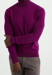 Pull à col roulé violet en coupe slim avec poignets et ourlet côtelés ; texture lisse avec une silhouette ajustée, associé à un pantalon gris à motifs.