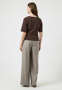 Top marrone a maniche corte con scollo rotondo, abbinato a pantaloni a gamba larga grigi chiari. Il tessuto appare liscio con una vestibilità strutturata.