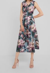 Blommig ärmlös klänning i teal-tyg, med stora rosa och vita rosor, åtsittande liv, plisserad kjol och längd till mitten av vaderna.