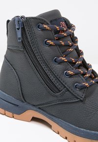 Scarponi da trekking in pelle nera con lacci arancioni, cerniera laterale e suola robusta marrone, progettati per l'uso all'aperto.