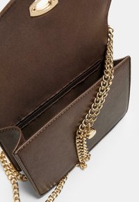 Smeđa kožna torba preko tijela s naramenicom od zlatnog lanca, s unutarnjim džepom na patentni zatvarač i magnetnim kopčanjem sprijeda.