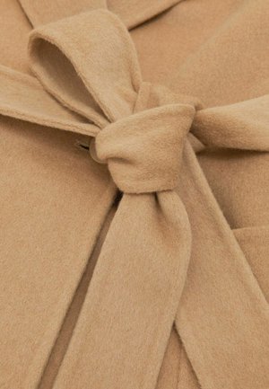 Kamel gyapjú kabát, övcsomóval megkötve, alatta látható gombbal, puha textúrájú anyagon.