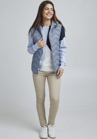 Vest dinamic, bleu deschis, matlasat, cu glugă, asortat cu un pulover bleu deschis și bleumarin, pantaloni bej și adidași albi. Design simplu și elegant.
