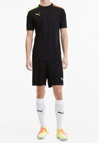 Svart sporttröja med korta ärmar, med färgdetaljer i grönt och orange på axlarna. Matchas med svarta shorts, vita strumpor och ljusa fotbollsskor.