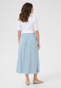 Lys blå, krøllet midi nederdel med en samlet talje og sideslids, parret med en tætsiddende hvid top og beige flade sko.