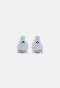 White soccer cleats with a mesh upper, clear plastic sole, blue three-stripe logo, and a rounded design. Subtle texture on the upper surface.