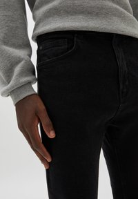 Jeans de mezclilla negra con un diseño ajustado, que cuentan con bolsillos frontales y costuras mínimas. La tela parece suave con un ligero brillo.