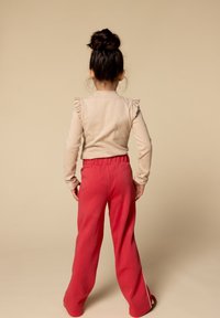 Beige lange mouwen top met ruffle accenten en rode wijde broek met elastische tailleband. Glad materiaal en een relaxte pasvorm.