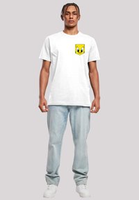 Hvit bomull T-skjorte med korte ermer, med et gult Tweety Bird lommegrafikk. Brukt sammen med lyse denimjeans og hvite joggesko.