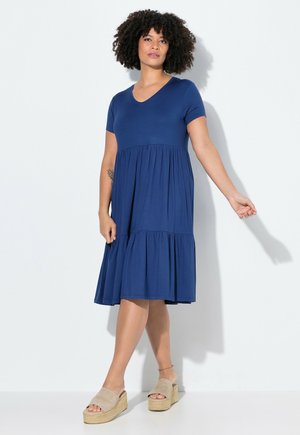 Navy blue short-sleeve dress with a V-neck, tiered skirt, and soft fabric. Worn with beige platform sandals. Simple, flowing design.