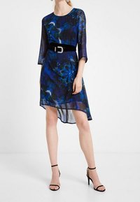 Blaues Blumenkleid aus durchsichtigem Stoff, mit rundem Halsausschnitt, Dreiviertelärmeln und einem schwarzen Samtgürtel mit glänzender Schnalle.