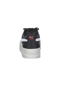 Scarpa sportiva in bianco e nero con tomaia nera imbottita, tallone testurizzato, intersuola bianca e dettagli del logo Puma in oro e rosso.
