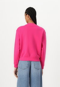 Sudadera de color rosa brillante con mangas largas, puños y dobladillo acanalados. Combinada con pantalones cortos de mezclilla azul claro que tienen bolsillos traseros.