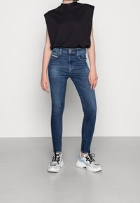Mörkblå skinny jeans med hög midja, kombinerat med en svart ärmlös topp och vita sneakers med svarta och ljusblå accenter.