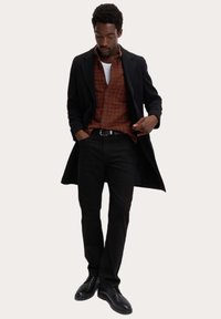 Abrigo negro, camisa a cuadros marrón, camiseta blanca, pantalones negros y zapatos negros. Tejido suave con un corte a medida.