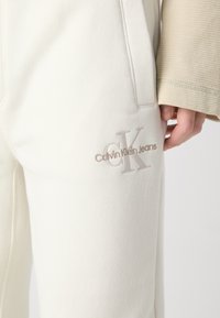 Fehér, puha pamut keverékből készült melegítőnadrág, a bal combon világos bézs színű, hímzett Calvin Klein logóval.