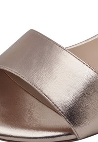 Sandale à glissière en métal rose doré avec large bande, texture lisse et design à bout ouvert. Caractéristiques : lignes épurées et détails de couture subtils.
