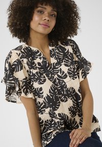 Blusa a stampa floreale in beige con grandi motivi di foglie tropicali nere, con scollatura a V e maniche a volants, realizzata in tessuto leggero.
