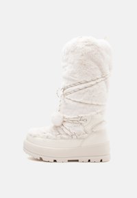 White faux fur knee-high boot with a chunky white sole, decorative laces, and a pom-pom accent at the top. Soft texture throughout.