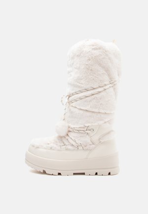 White faux fur knee-high boot with a chunky white sole, decorative laces, and a pom-pom accent at the top. Soft texture throughout.