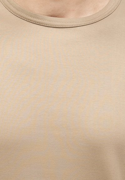 Μπεζ μπλούζα με στρογγυλή λαιμόκοψη που εμφανίζεται στο πάνω μέρος του στήθους και στον λαιμό ενός ατόμου με ανοιχτό τόνο δέρματος.