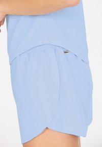 Hellblaue Sportshorts mit Netzstruktur und elastischem Bund; mit kurzem, gespaltenem Saum für Bewegungsfreiheit. Akzentuierung mit Beschlägen in Goldfarbe.