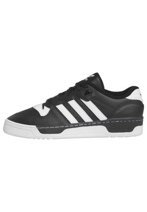 Zapatilla deportiva de corte bajo en blanco y negro con tres rayas blancas, cordones en la parte delantera y suela blanca texturizada.