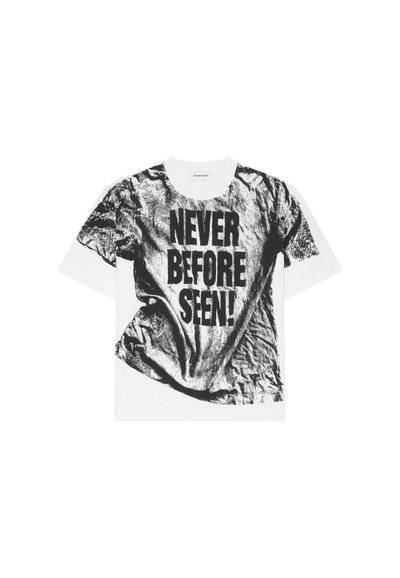 T-shirt blanc avec un imprimé graphique noir texturé et froissé, portant le texte "JAMAIS VU AVANT !" en lettres majuscules. Design à col rond.