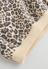 Løveprintsstof med nuancer af brunt, sort og beige, med en blød tekstur og en ribbet beige manchet nederst.