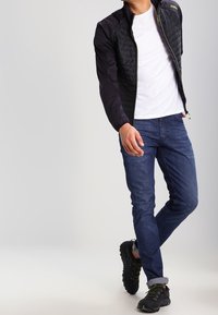 Sort quiltet jakke med elastiske manchetter, parret med denim jeans og sorte sneakers. Jakken har lynlås lukning og logo detalje.