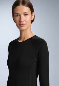 Black long-sleeve top with a round neckline, featuring a textured fabric and visible seam detailing, against a light grey background.