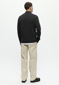 Pulover tricotat de culoare gri închis, cu un guler înalt, asociat cu pantaloni larghi de culoare crem. Încălțămintea are accente de culoare maro închis, cu o talpă texturată.