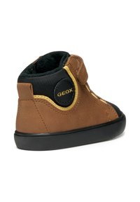 Chaussure montante en cuir marron avec des accents textiles noirs, bande Velcro, bout rond et semelle en caoutchouc. Présente un patch logo GEOX sur le côté.