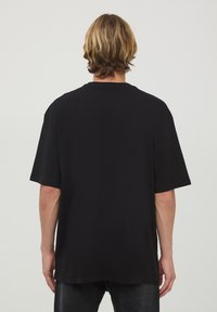 Czarna, oversize koszulka z bawełny, z krótkimi rękawami i okrągłym dekoltem. Gładka tekstura bez widocznych wzorów lub detali.